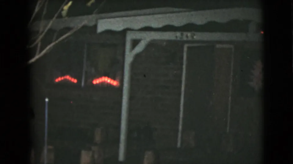 1968 8mm nighttime view of the Clarksdale house porch area, with red lights, doorway, posts, and dim yard objects.