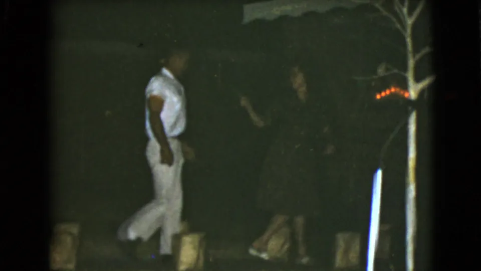 Near the end of the 1968 Clarksdale, Arizona clip, two men move past a bare tree and faint red lights in a dark outdoor home-movie scene.