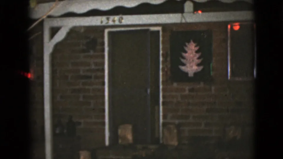 The brick house exterior remains in view after the figures have disappeared, with the door closed and the tree decoration beside it.