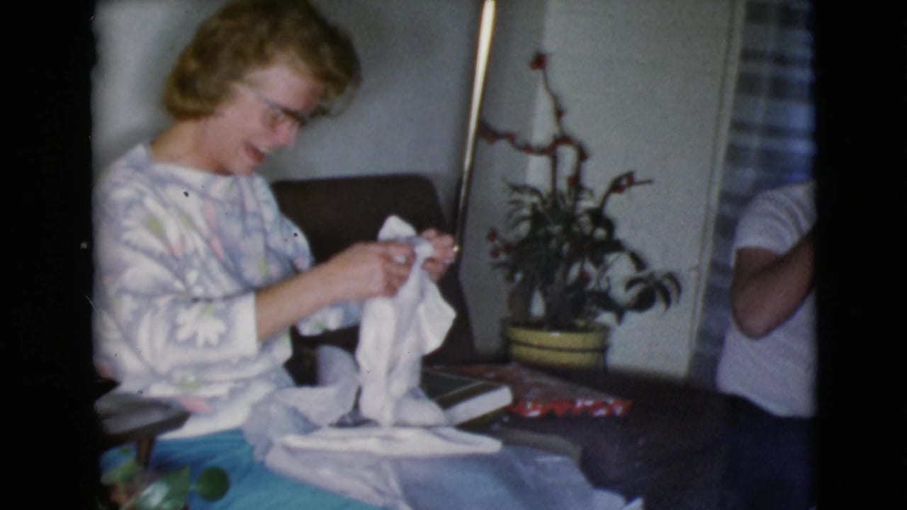 Woman in glasses sits on a couch holding a white cloth gift.