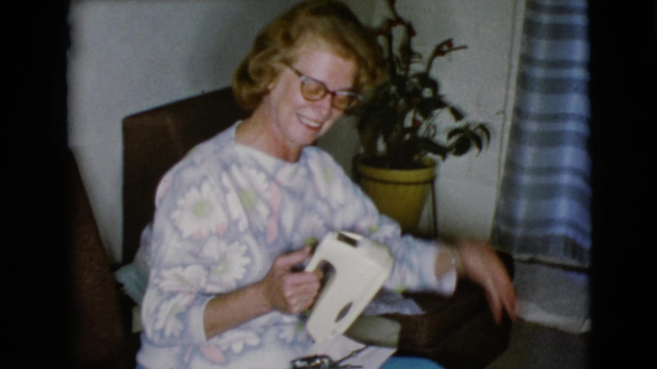 A smiling woman in glasses holds a white household object or gift in this 1968 Clarksdale, Arizona Christmas home-movie frame.