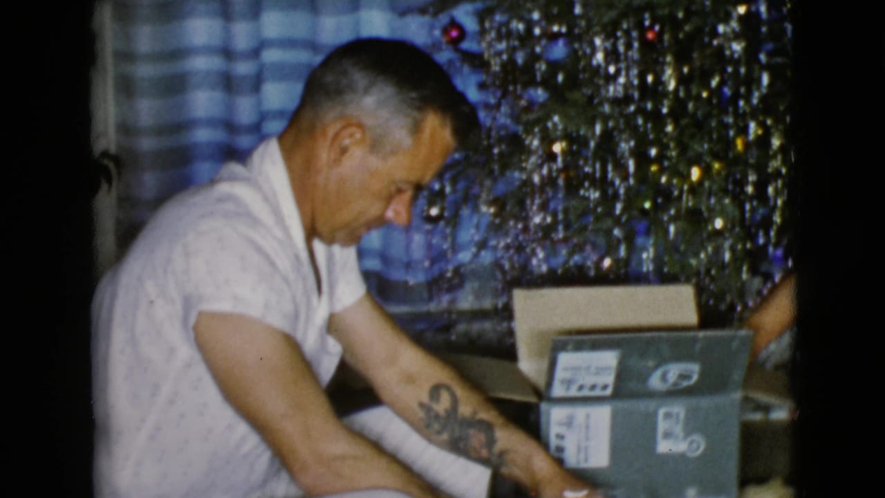 The father leans toward the present while a family member's arm reaches near a labeled box in the 1968 holiday interior.