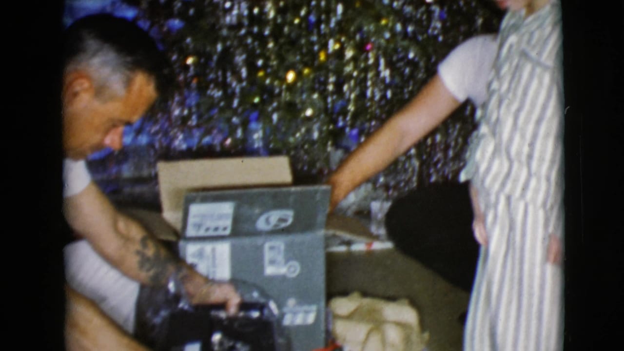 The final frame shows the father handling the present near a labeled box, with another person partly visible beside the tinsel tree.