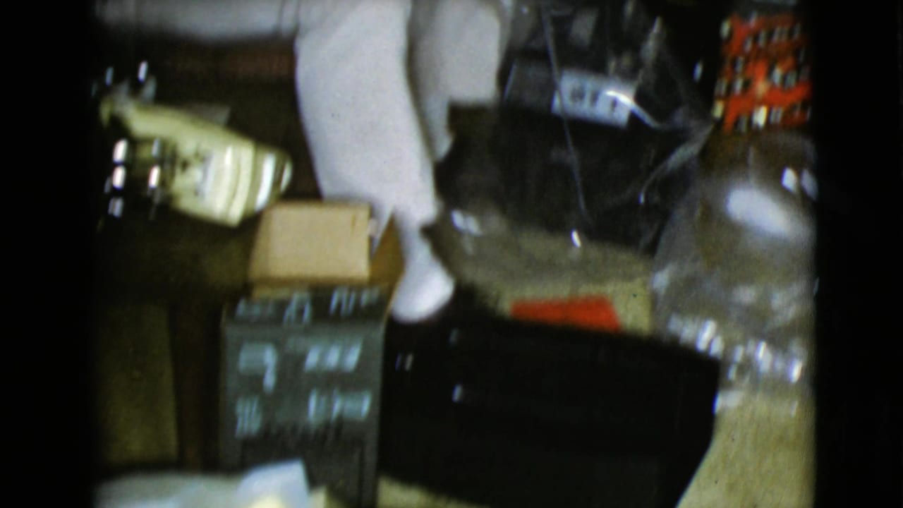 A floor-level 8mm frame shows Christmas packages, a box, a pale object, and household items inside a private interior.