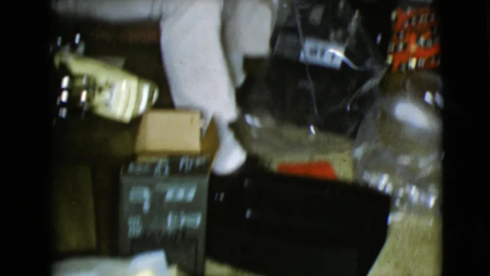 A floor-level 8mm frame shows Christmas packages, a box, a pale object, and household items inside a private interior.