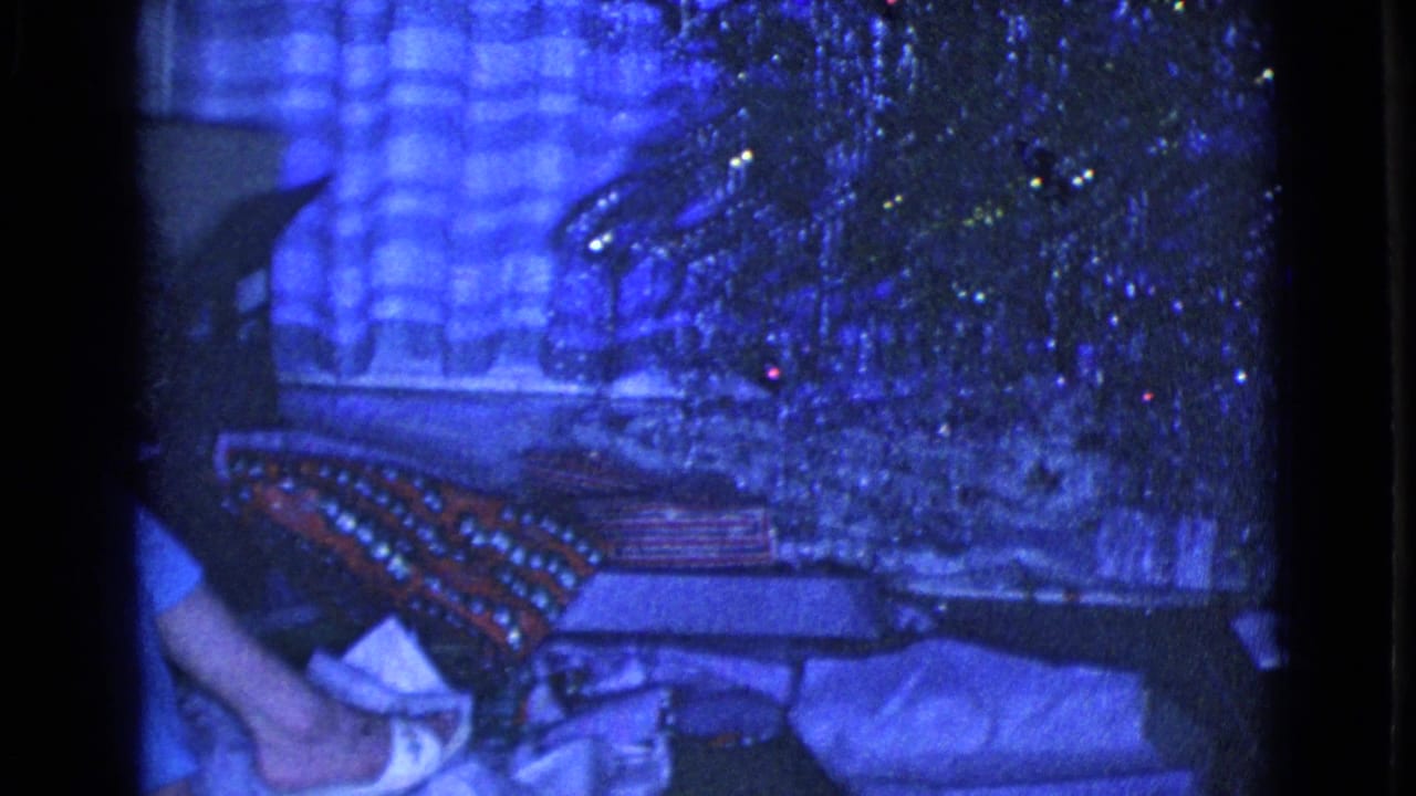 Wrapped gifts and a tinsel Christmas tree beside plaid curtains in a dim room.