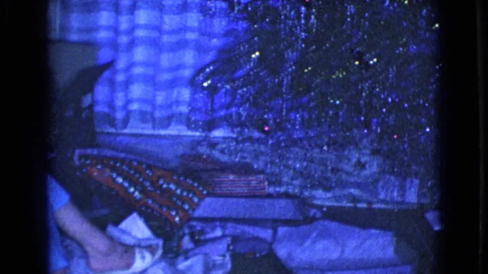 1968 Clarksdale, Arizona frame with wrapped presents beneath or near a tinsel Christmas tree in a blue-tinted private living room.