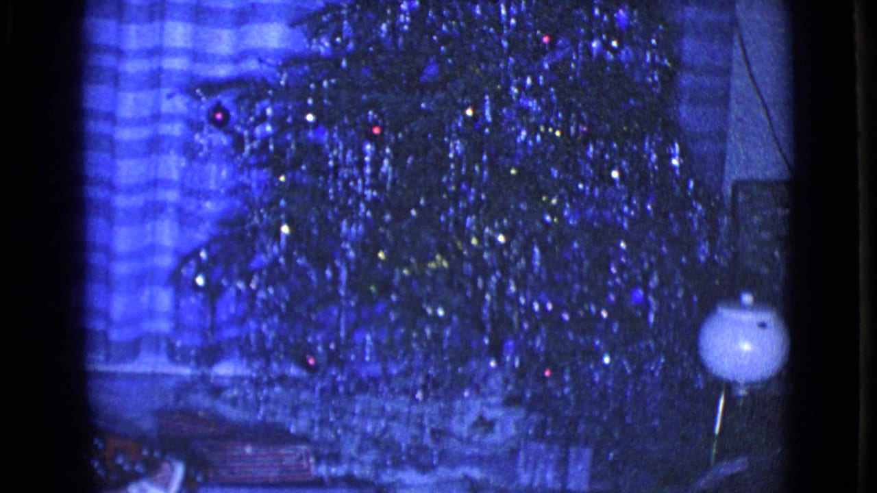 1968 Clarksdale, Arizona home-movie frame centered on a silver tinsel Christmas tree with ornaments, gifts, curtains, and a floor lamp.