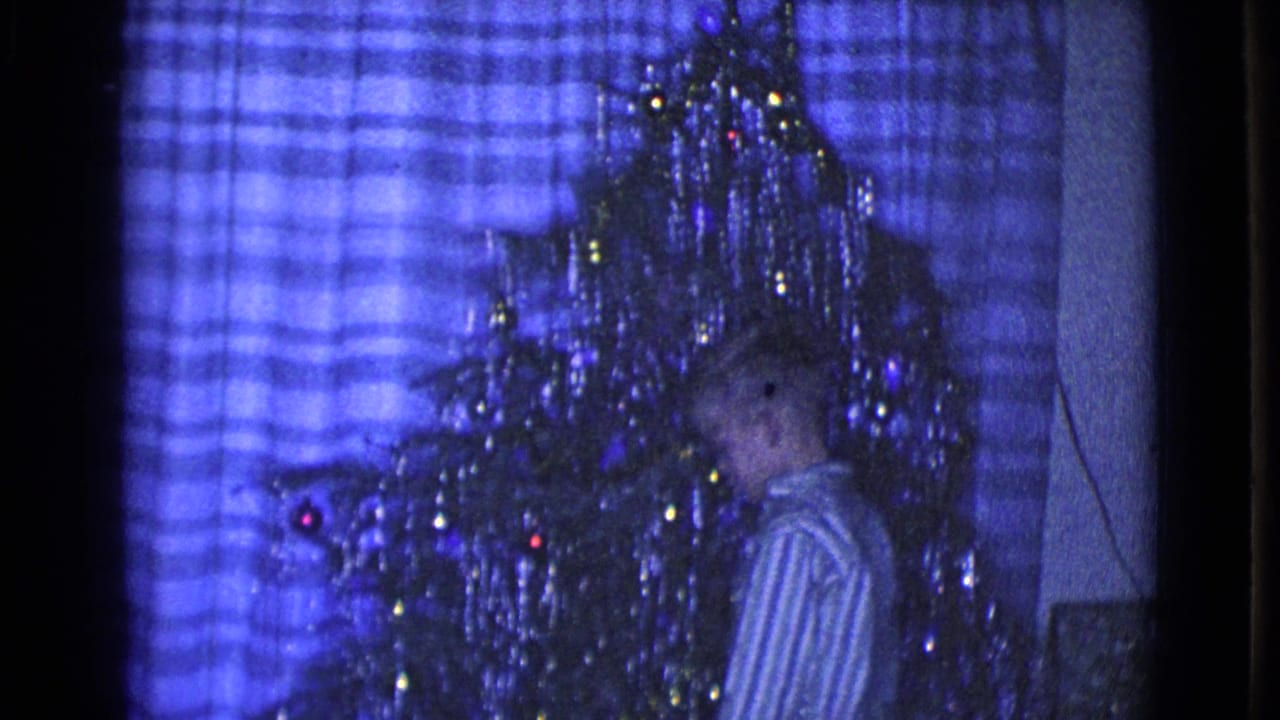 1968 Clarksdale, Arizona frame showing a child beside a decorated tinsel Christmas tree in a private blue-lit living room.