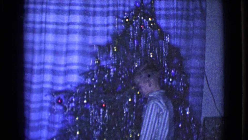 1968 Clarksdale, Arizona frame showing a child beside a decorated tinsel Christmas tree in a private blue-lit living room.