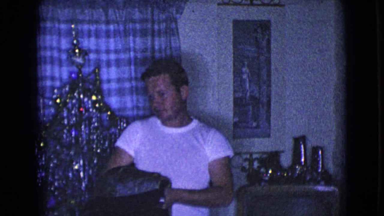Man holds a dark garment in front of a Christmas tree and plaid curtain.