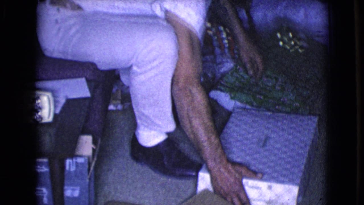The man sits and reaches toward items on the floor, with the Christmas tree and household furnishings partly visible around him.