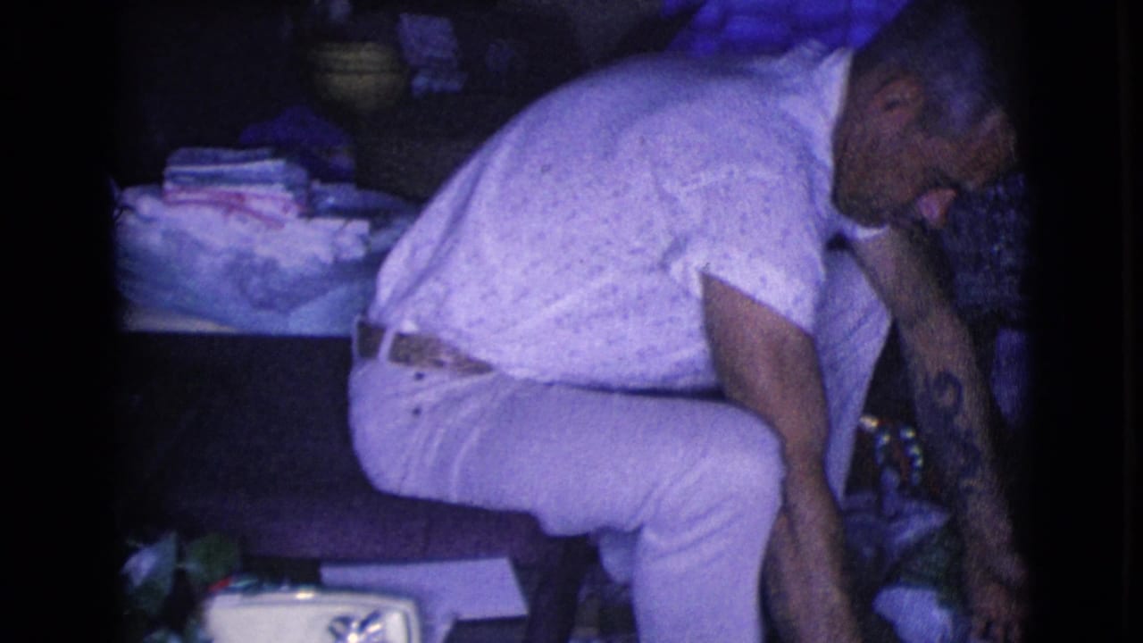 The man bends down from a chair toward packages or a box on the floor in the dim Christmas living-room setting.