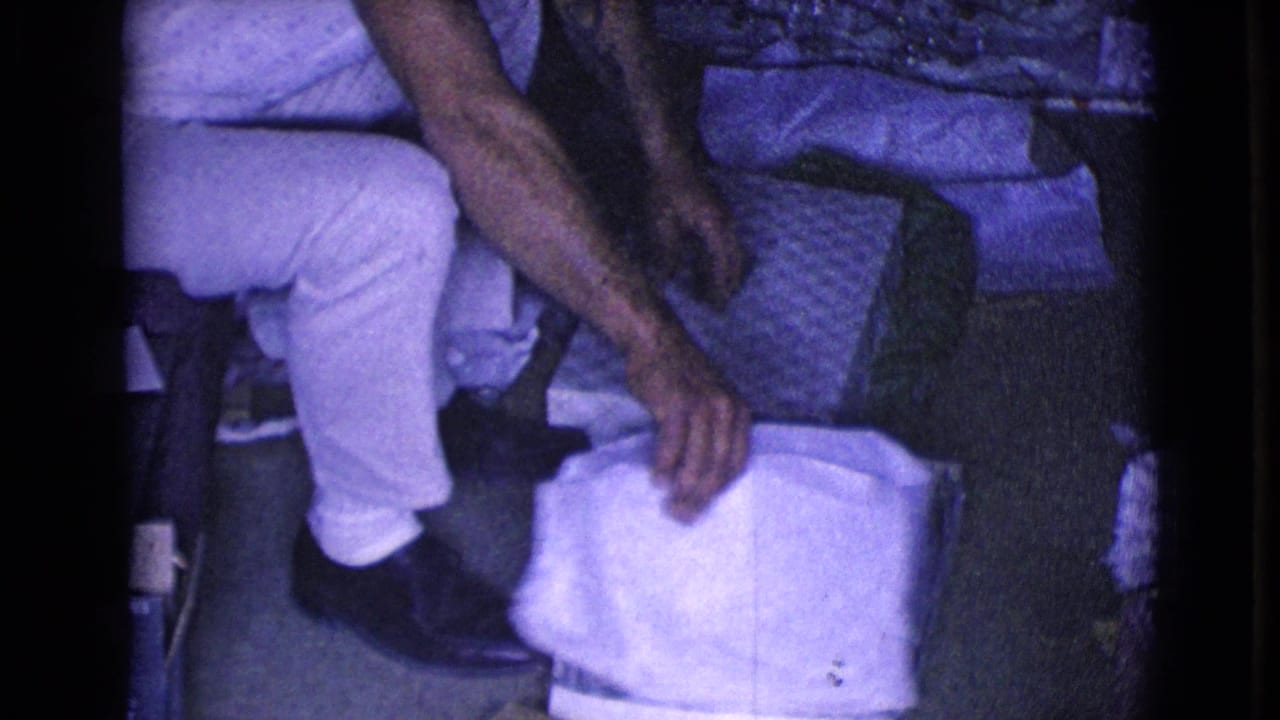 The seated young man leans forward toward white paper near his feet while the opened gift materials rest beside him.