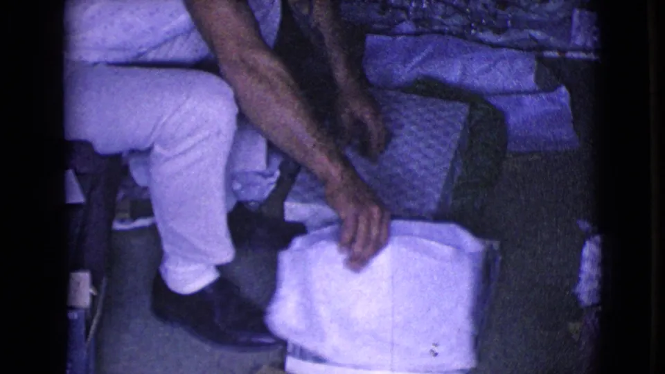 The seated young man leans forward toward white paper near his feet while the opened gift materials rest beside him.