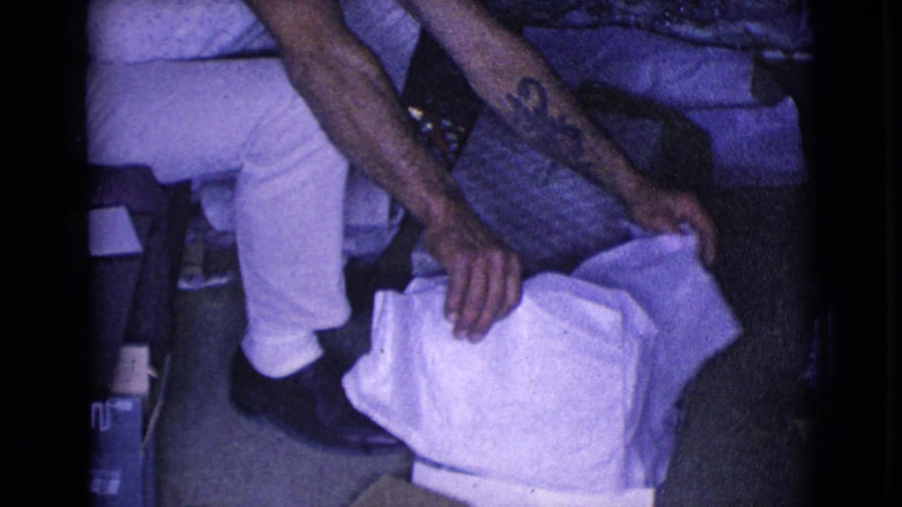 The young man remains seated in the private interior, with a textured box and loose white paper visible beside his legs.