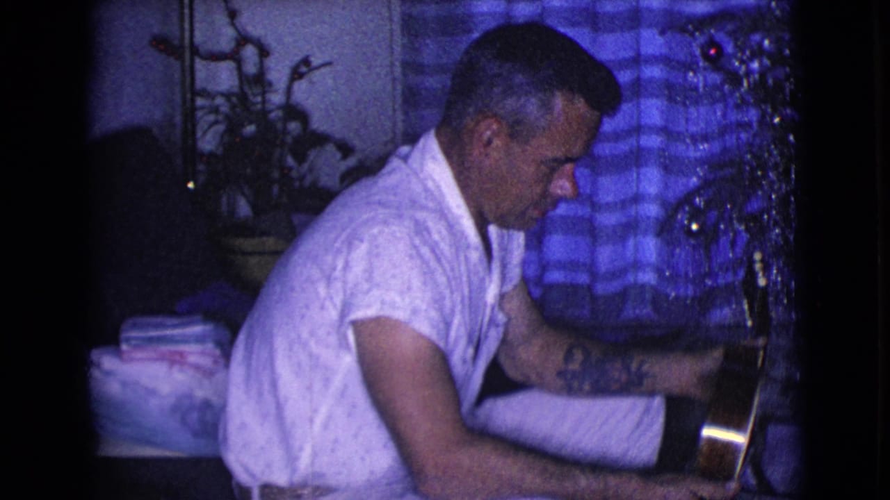 The home-movie frame from Clarksdale, Arizona in 1968 shows the man looking down at the instrument, with tinsel and curtains behind him.