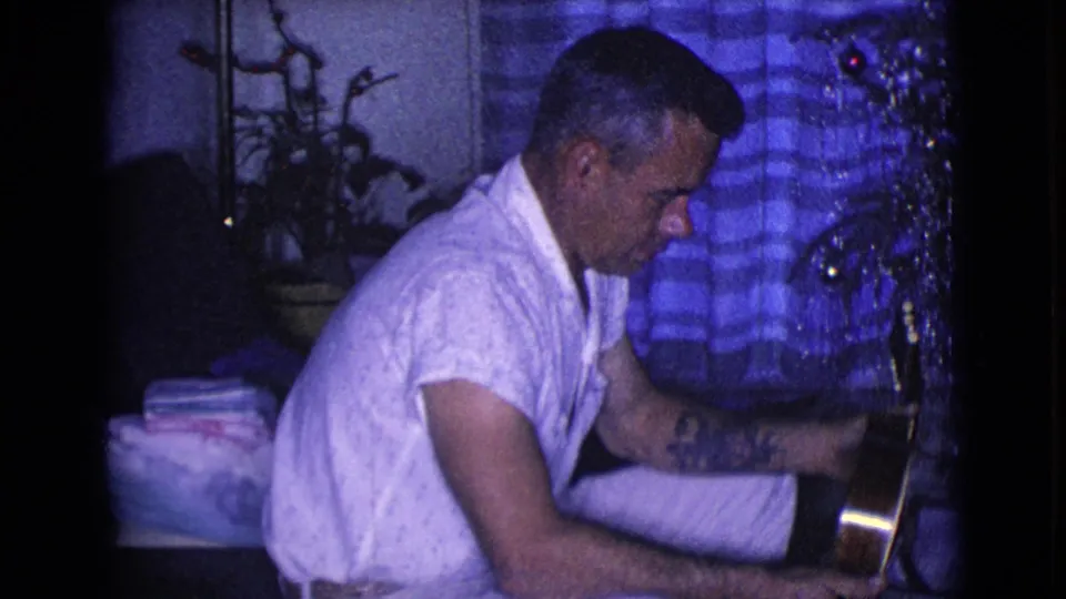 The home-movie frame from Clarksdale, Arizona in 1968 shows the man looking down at the instrument, with tinsel and curtains behind him.