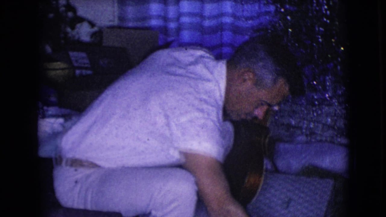 A 1968 home-movie frame shows the man bending forward indoors near the Christmas tree, with the small instrument partly visible at his side.