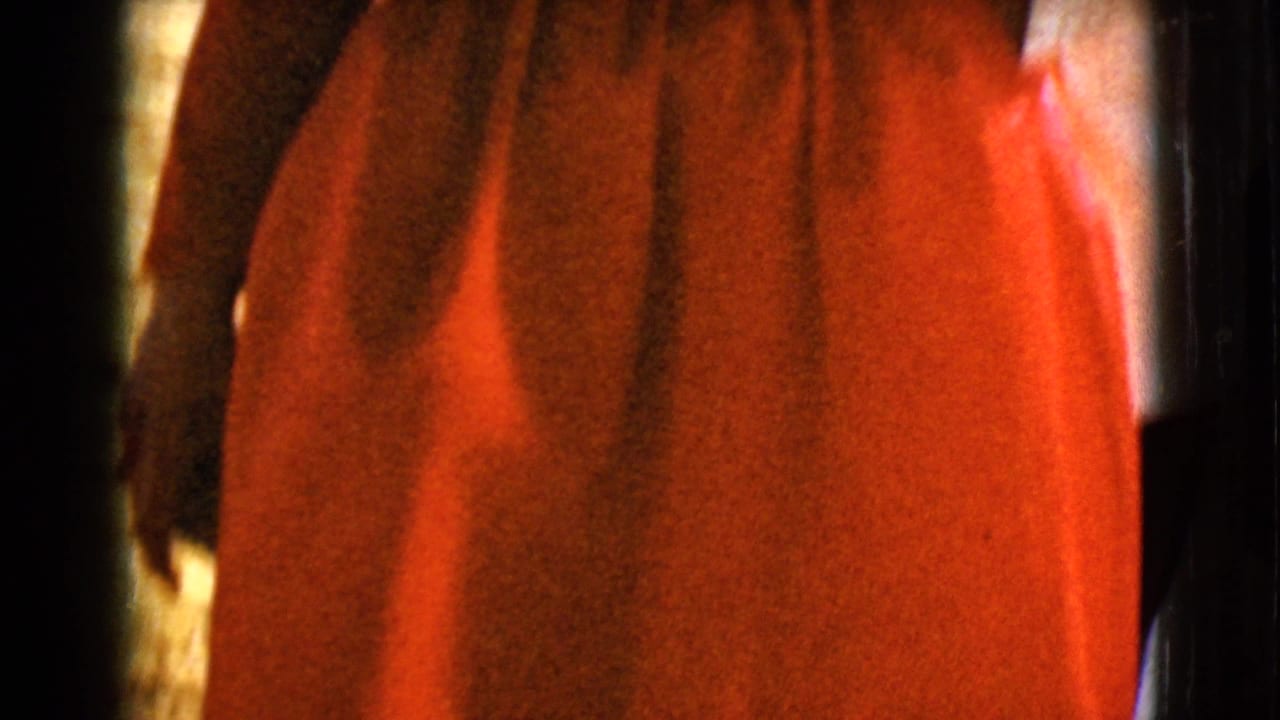 A close 8mm frame shows the red fabric of the woman's formal dress, with the figure mostly cropped.