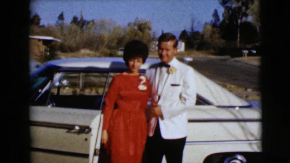 The formally dressed couple poses beside a light-colored classic American car in a sunny Clarksdale, Arizona roadside setting.