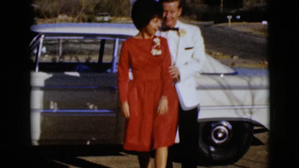 In the final frame, the couple stands arm in arm beside the classic car, with the woman in red and the man in a white jacket.