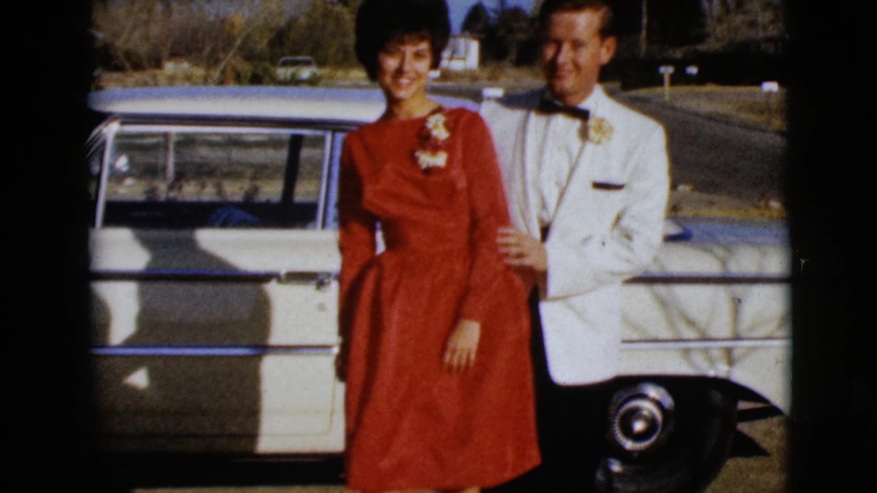 In 1968 Clarksdale, Arizona footage, a couple poses beside a white car, with the woman in a red dress and the man in a white tuxedo jacket.