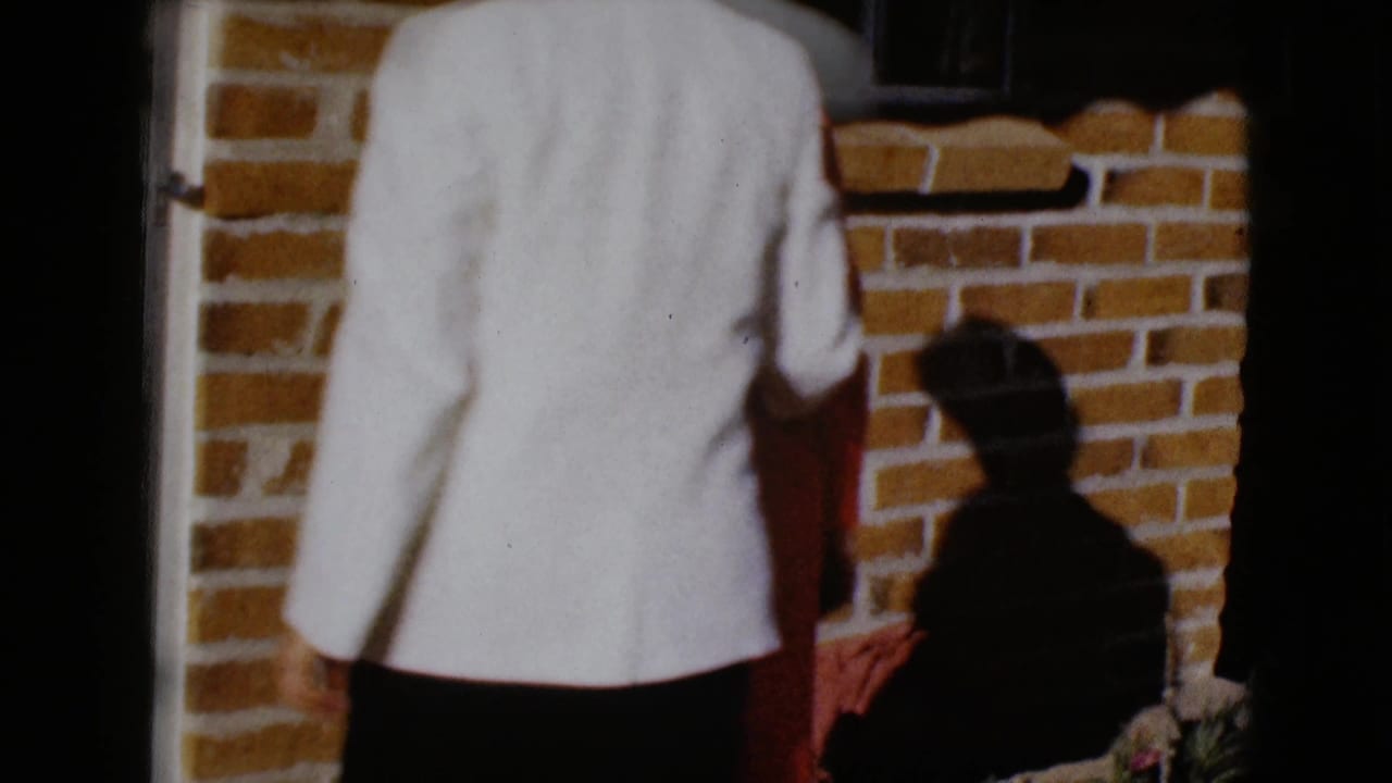 A person in a light jacket stands with their back to the camera on a brick porch.