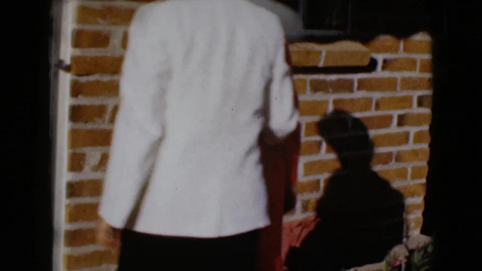 1968 8mm frame from Clarksdale, Arizona showing a light-jacketed figure from behind near a brick porch and doorway.