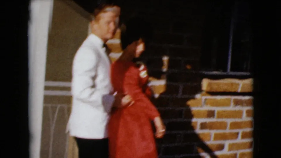 In this 1968 Clarksdale, Arizona home-movie frame, a formally dressed couple poses together on a sunlit brick porch.