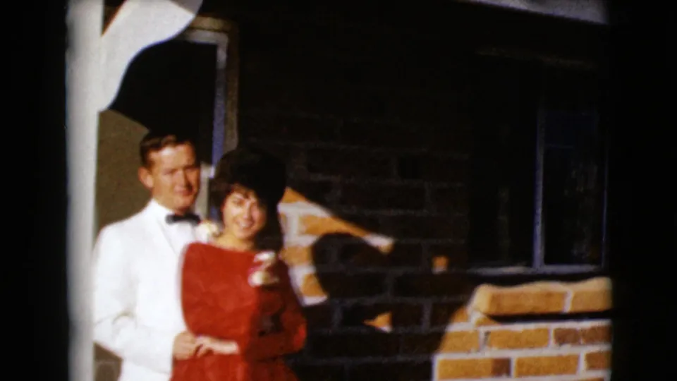 The couple smiles toward the camera in 1968 Clarksdale, Arizona, standing close on a brick porch in formal clothing.