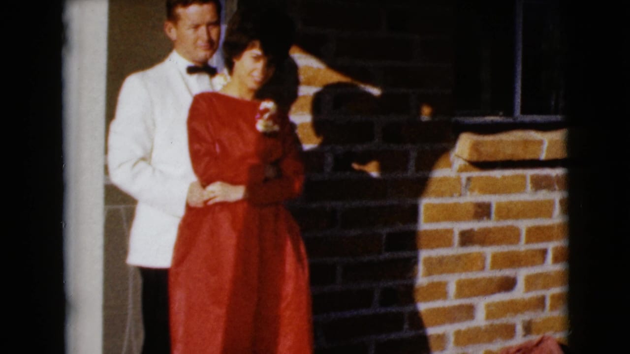 Adult couple posing by a doorway, with the man in a white jacket and the woman in a red dress.