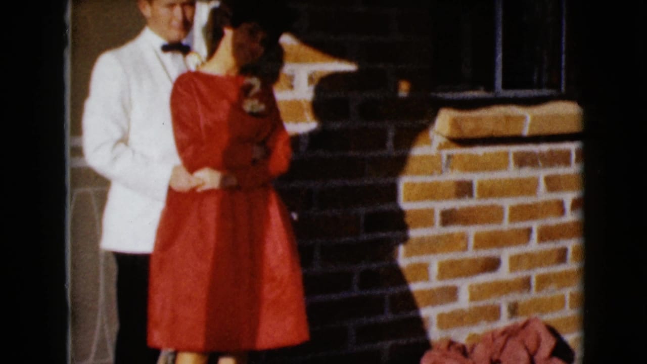 The couple turns slightly toward each other while standing beside a brick wall and doorway.