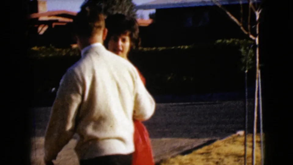 1968 Clarksdale, Arizona frame showing an adult man and woman walking together near a quiet suburban street.