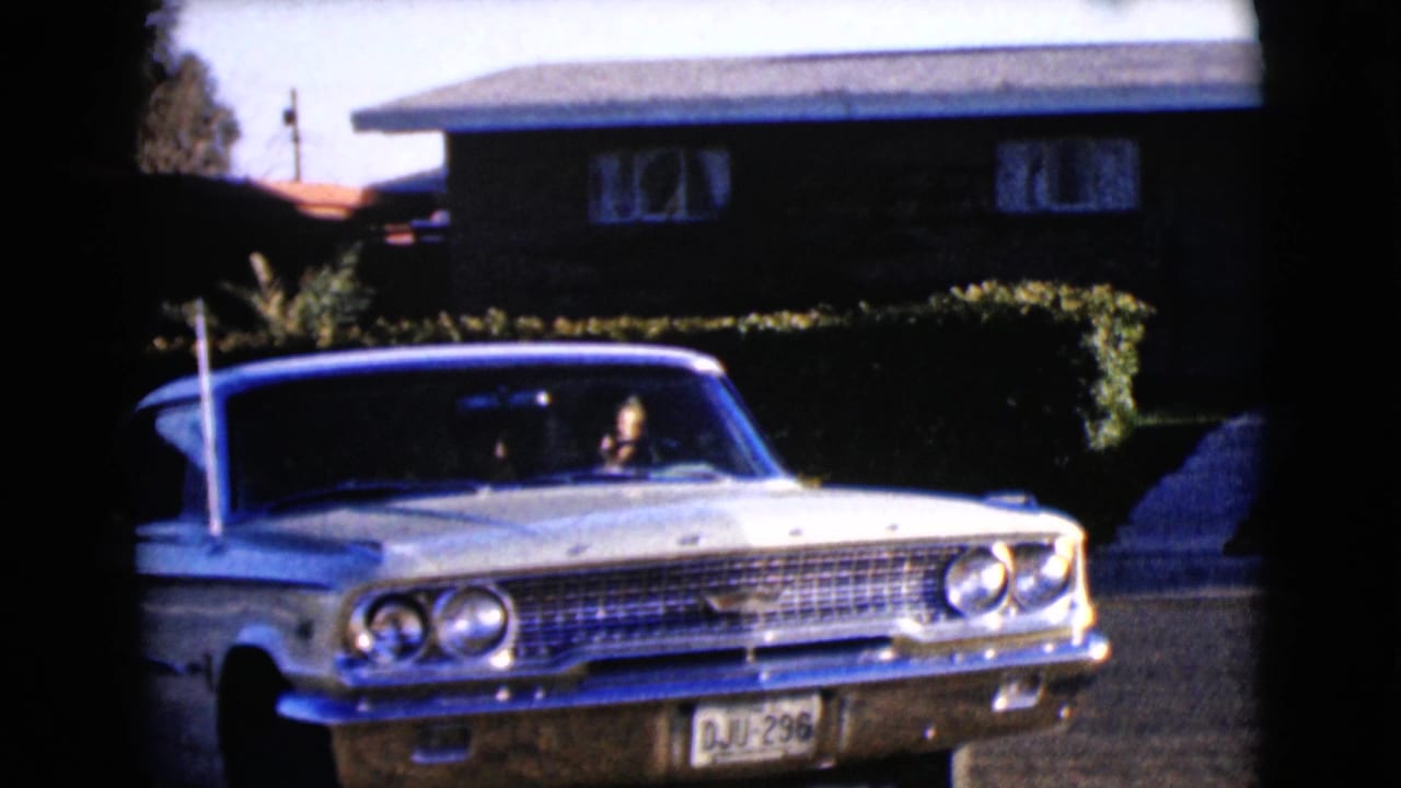 1968 Clarksdale, Arizona frame of a white classic sedan backing or turning from a driveway, with the driver visible and the front plate readable.