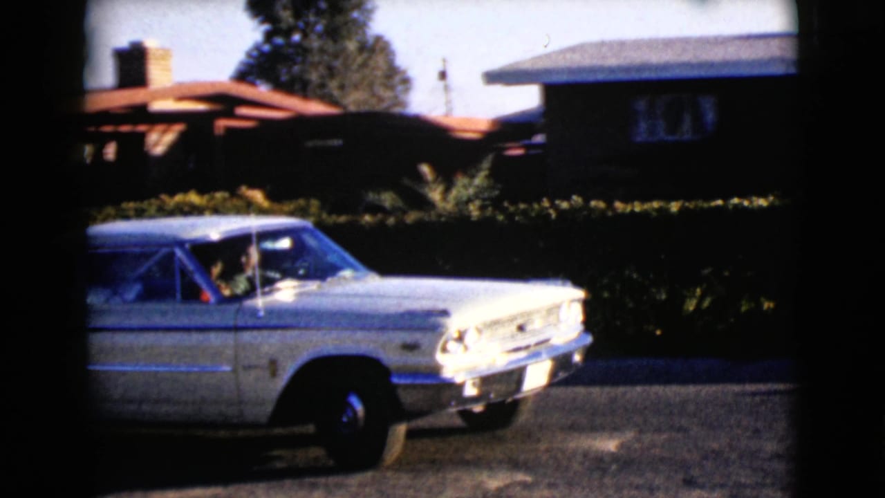 White vintage sedan partly in frame on a sunny residential street.