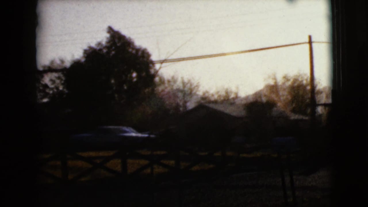 Darkened roadside view with a car silhouette near fencing, trees, and utility lines.
