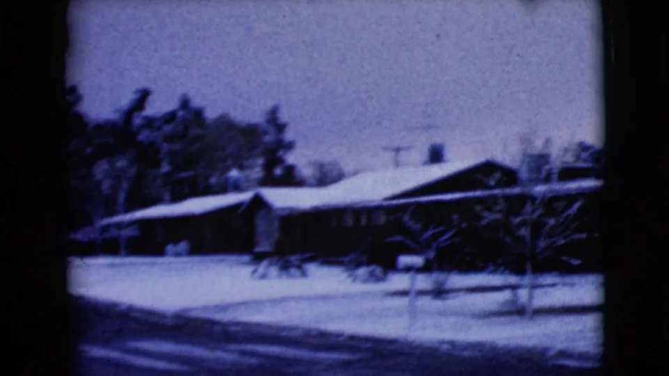 A snow-covered residential house and yard appear across the street, continuing the archival 1968 home-movie view of the neighborhood.