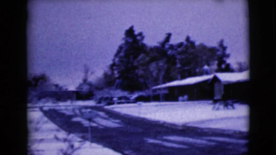 A snowy neighborhood road leads past residential homes and trees in the final frame of the 1968 8mm home-movie clip.