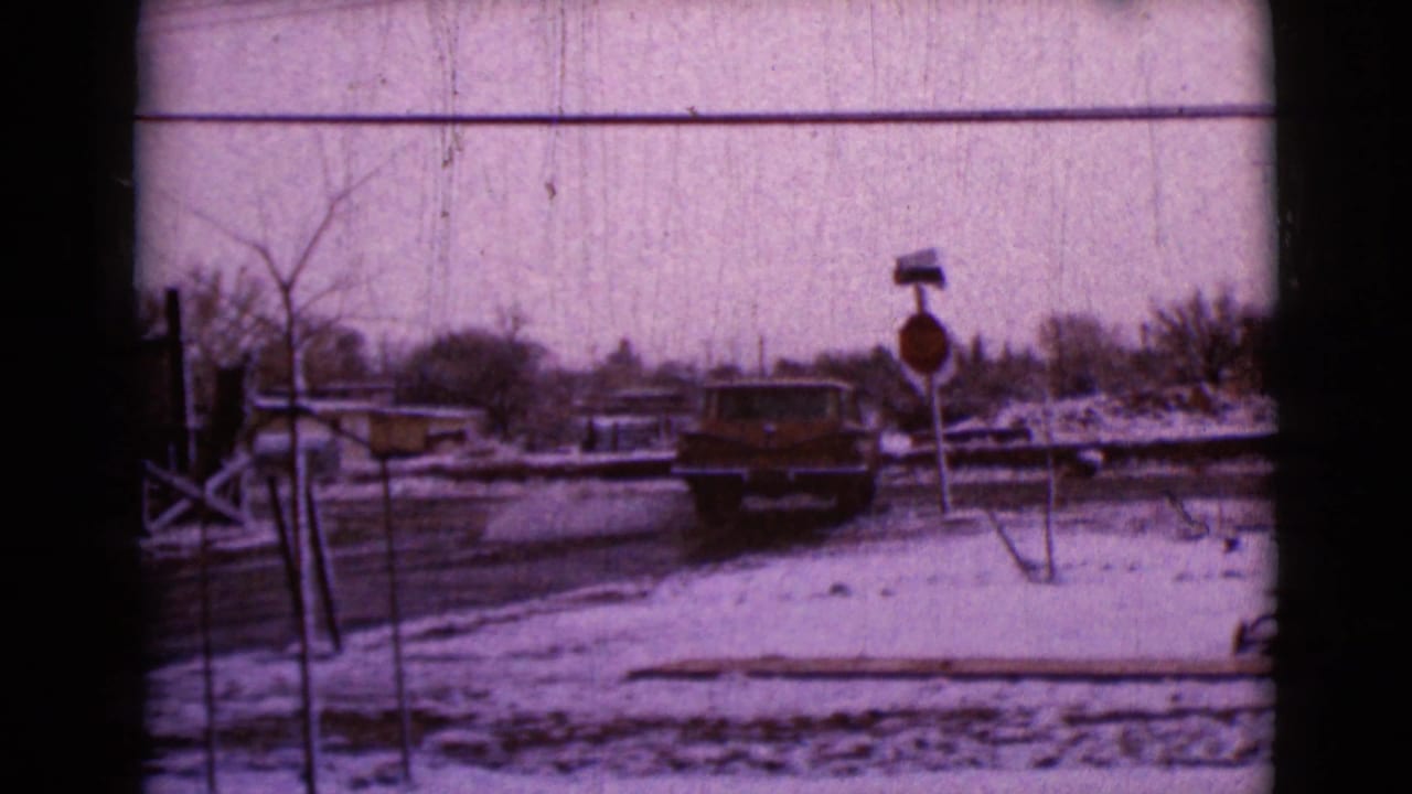 1968 Clarksdale, Arizona home-movie frame showing a dark car on a snowy residential road near a stop sign and utility lines.