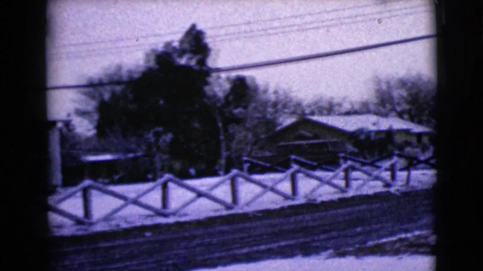 1968 Clarksdale, Arizona frame showing a snow-lined residential street edge, fence, trees, overhead wires, and houses in soft 8mm focus.