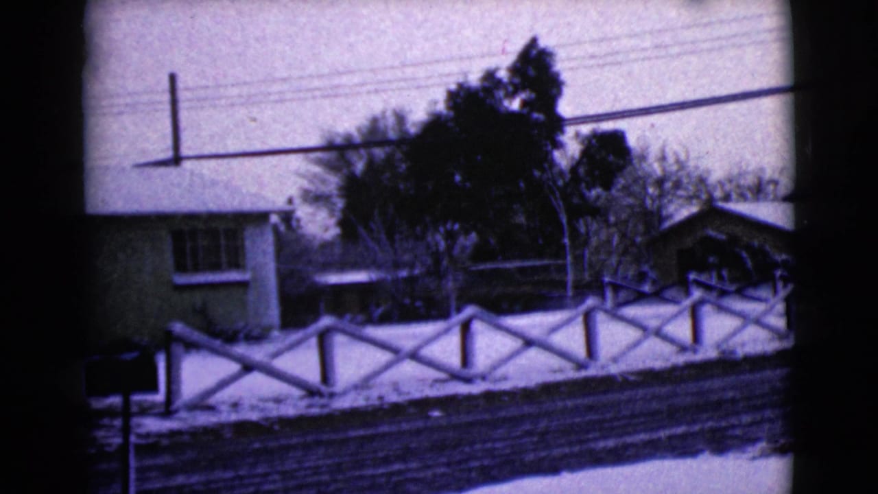 1968 8mm view of a snow-dusted residential street in Clarksdale, Arizona, with a modest house and white X-pattern fence.