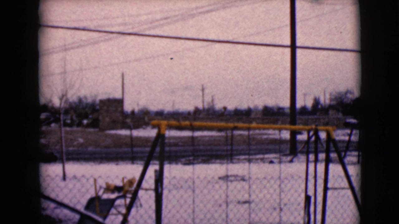Chain-link fenced playground with a yellow swing set on snowy ground.