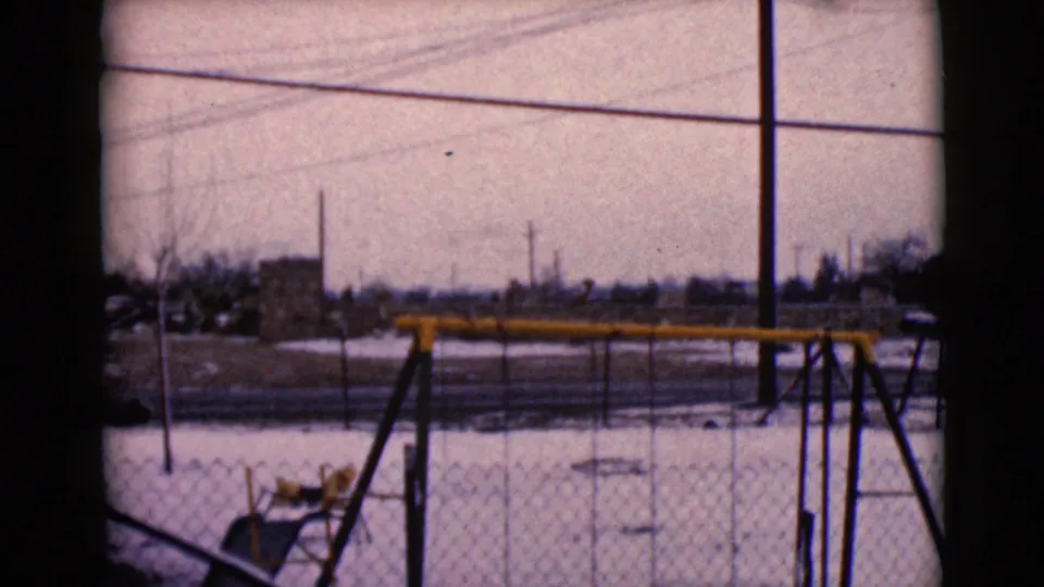 1968 8mm frame from Clarksdale, Arizona, showing an empty fenced playground with a yellow swing set, snow, and utility lines.