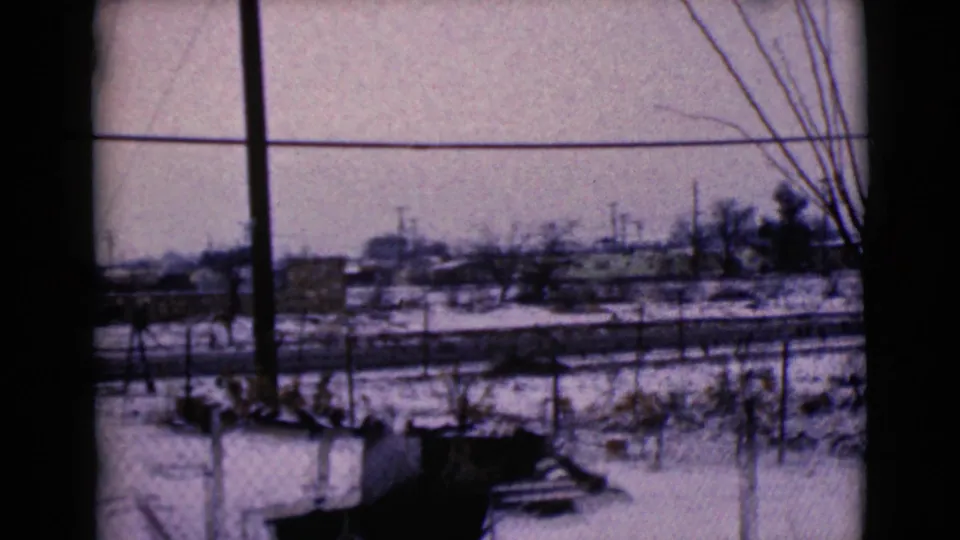 1968 8mm view in Clarksdale, Arizona, showing snowy fenced ground, bare branches, utility poles, and low buildings in the distance.