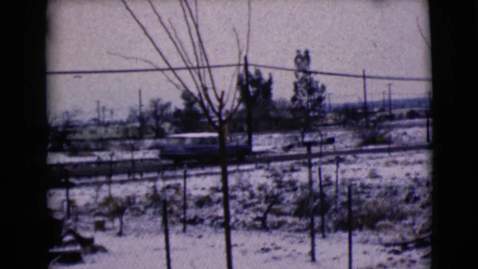 1968 home-movie frame of a car moving along a snow-dusted Clarksdale, Arizona road, partly obscured by bare trees and wires.