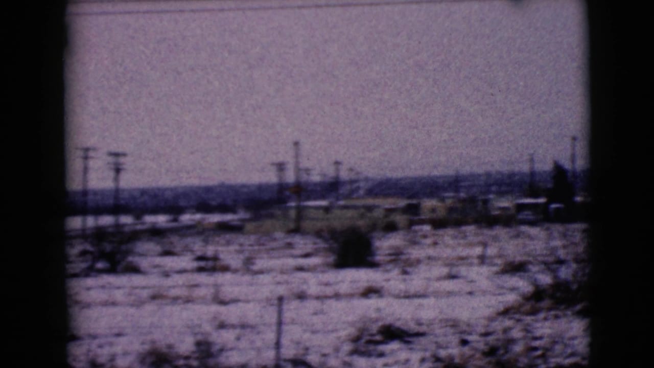 1968 Clarksdale, Arizona view of snow-covered terrain with utility poles, sparse brush, and low buildings in the distance.