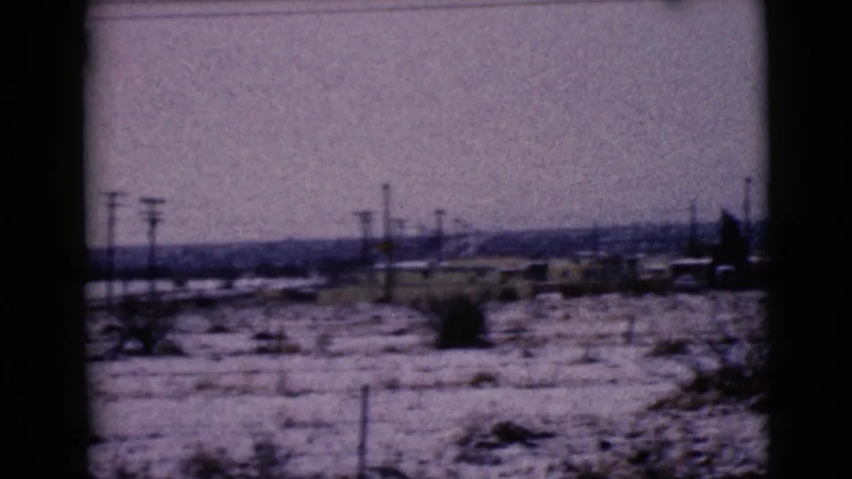 1968 Clarksdale, Arizona view of snow-covered terrain with utility poles, sparse brush, and low buildings in the distance.
