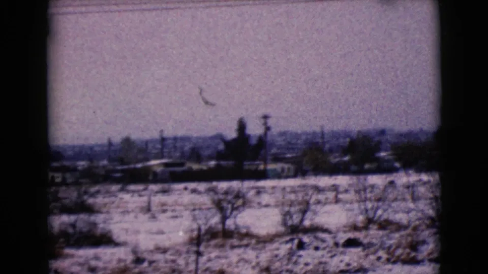 1968 Clarksdale, Arizona frame showing snow-dusted ground, bare trees, a utility pole, distant structures, and low hills.