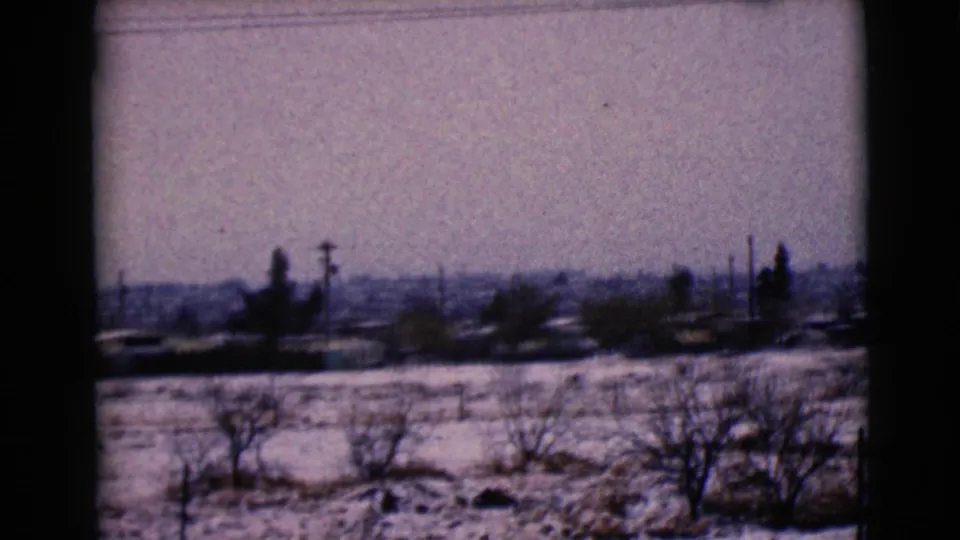 1968 8mm view of a snowy Clarksdale, Arizona landscape with bare trees, utility poles, distant houses, and a window frame in the foreground.